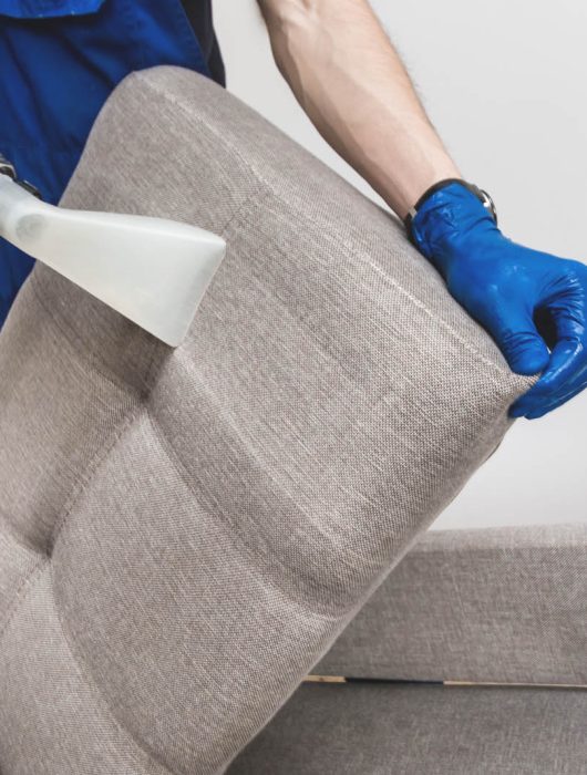 Cleaning service. Man janitor in gloves and uniform vacuum clean sofa with professional equipment