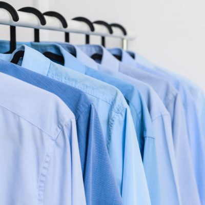 Rack with clothes after dry-cleaning near white wall, closeup